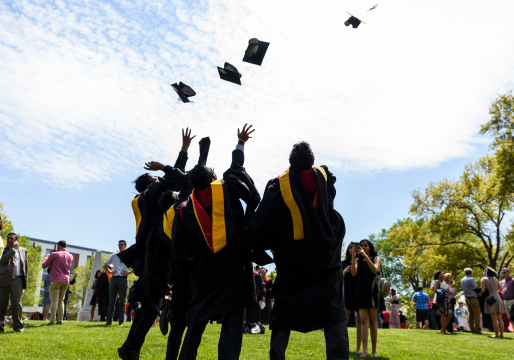 View of three students in graduation gowns tossing their caps into the air as they all look upwards.